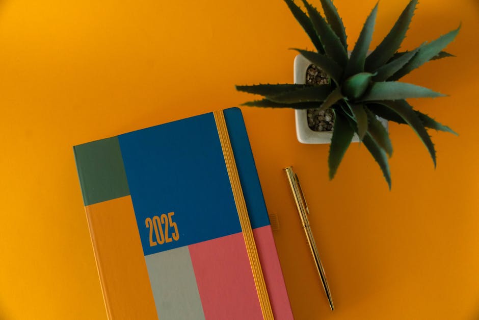 Colorful 2025 planner with gold pen and plant on yellow background.