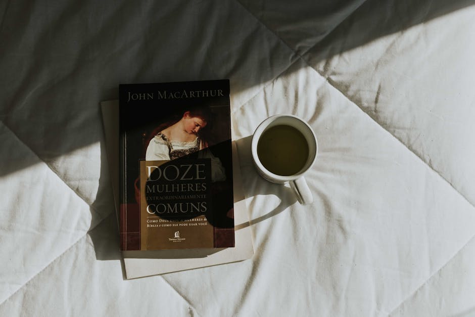 A book and cup of tea placed on a sunlit bedspread, creating a cozy and relaxed atmosphere.