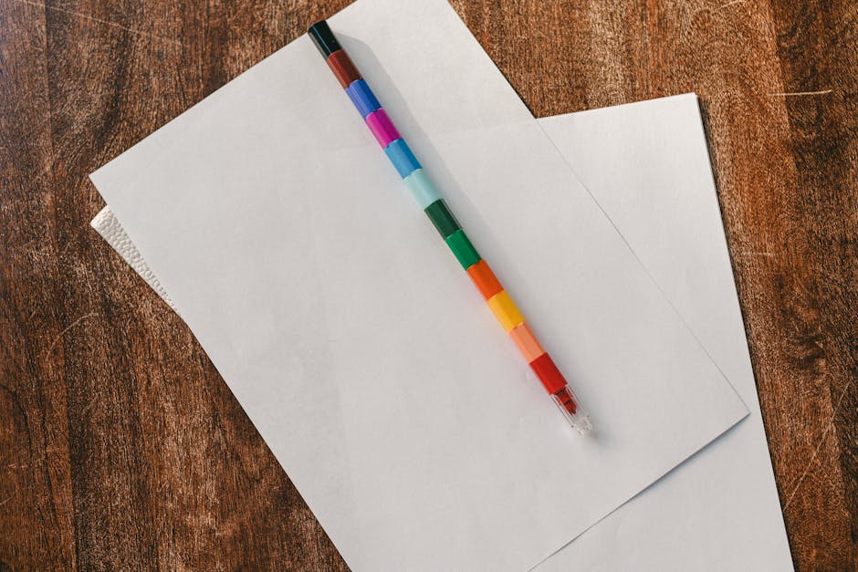 A vibrant multicolored pencil on white blank papers atop a rustic wooden desk.